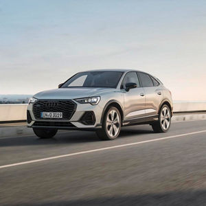A silver Audi Q3 driving on a smooth road under a clear sky, showcasing its modern design and performance.