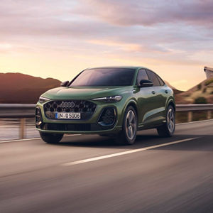 A green Audi Q5 Sportback driving on a scenic road with mountains and a sunset backdrop, showcasing its modern design.