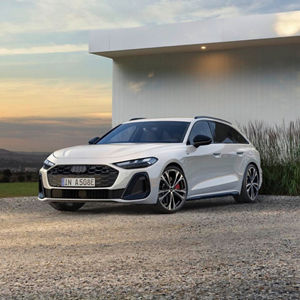 A white Audi A5 e-hybrid parked on gravel, with a modern building and gentle landscape in the background under a cloudy sky.