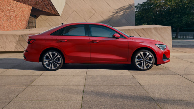 Red sedan Audi car parked on a sunny day near concrete structures.