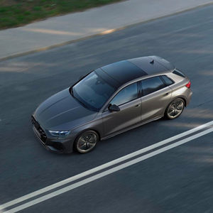 Aerial view of a grey Audi S3 Sportback driving on a dual-lane road, showcasing its modern design and glossy finish.