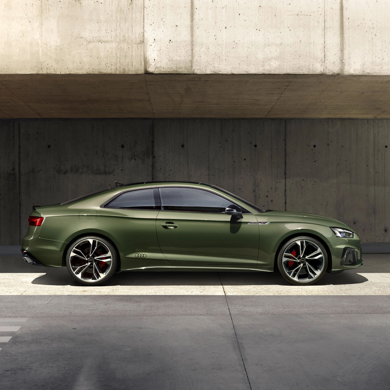 Green coupe car parked beside a concrete wall, with red brake callipers visible.