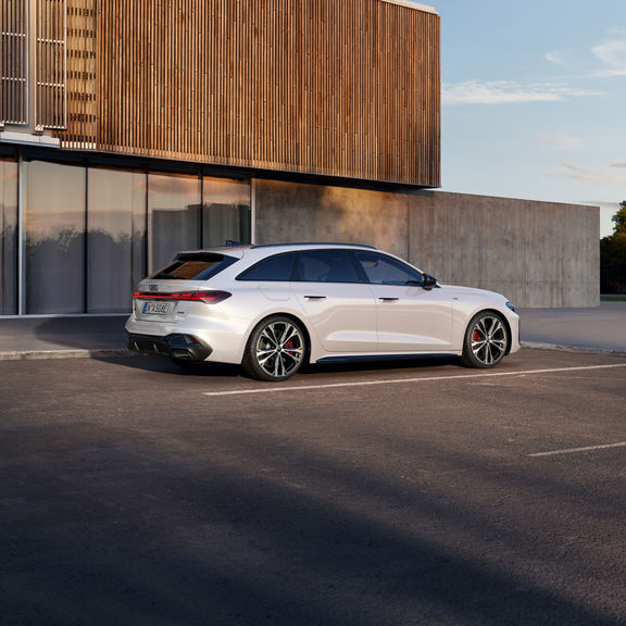 A sleek, white Audi e-hybrid is parked in an empty lot at dusk. The car's modern design features sharp lines and bold, red brake calipers.