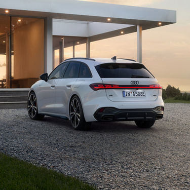 A sleek white Audi is parked on a gravel driveway beside a modern house at sunset.