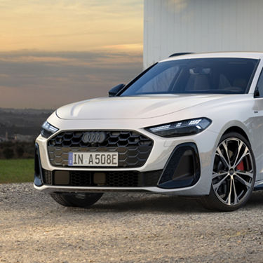 A sleek white Audi car parked on gravel, with sharp LED headlights and a prominent front grille. The setting is a serene sunset, enhancing the car's elegance.