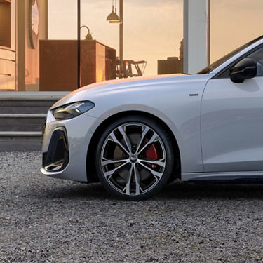 Close-up of a sleek silver car front, set against a modern building with large windows at sunset. The scene conveys elegance and sophistication.