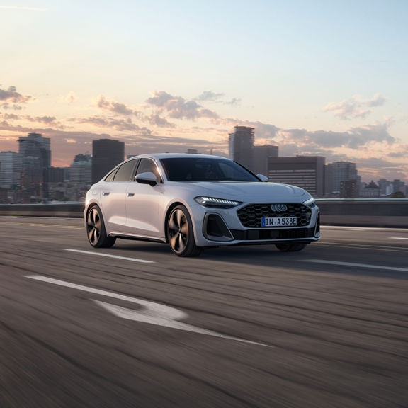 Silver car driving on an open highway at sunset, with a city skyline in the background.