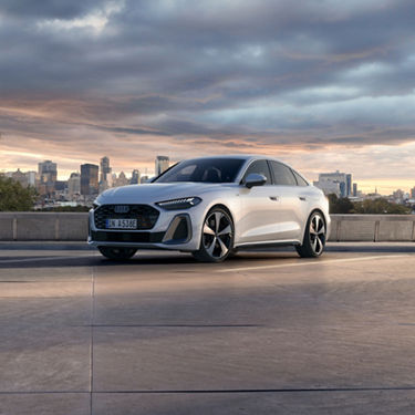 Sleek white sedan parked outdoors, against a city skyline at sunset. Modern design with angular headlights.