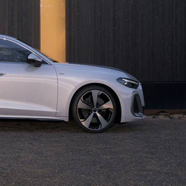 Silver car parked in front of a dark wooden wall, featuring sleek design and stylish wheels, conveying elegance and modernity.
