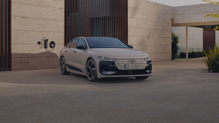 An Audi electric sedan driving along a coastal road at sunset.