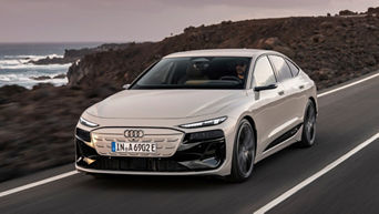 Audi A6 Sportback e-tron drives along a coastal road with rocky cliffs and ocean waves in the background, showcasing its sleek design.