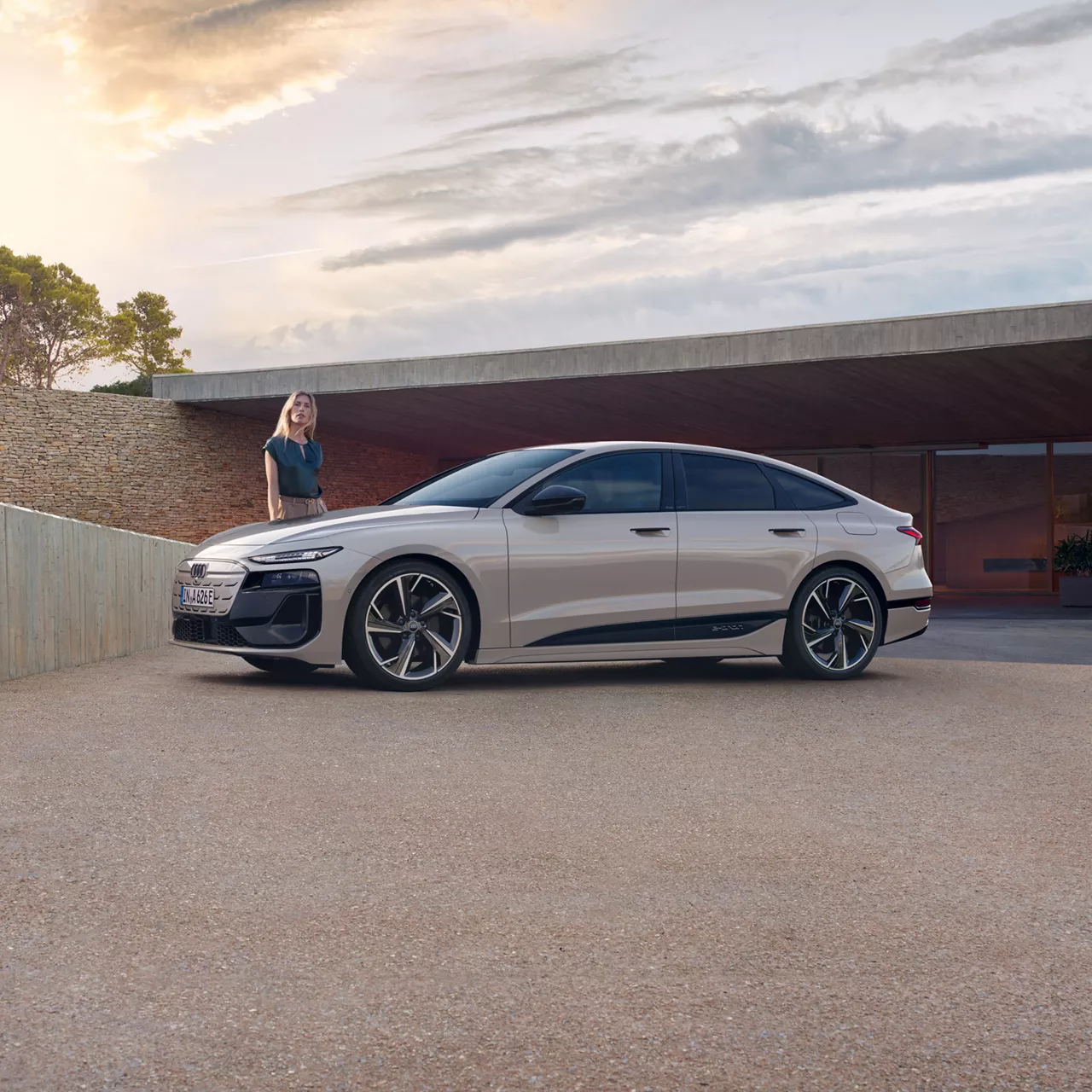 A sleek Audi electric sedan parked in front of a modern house with a woman beside it.