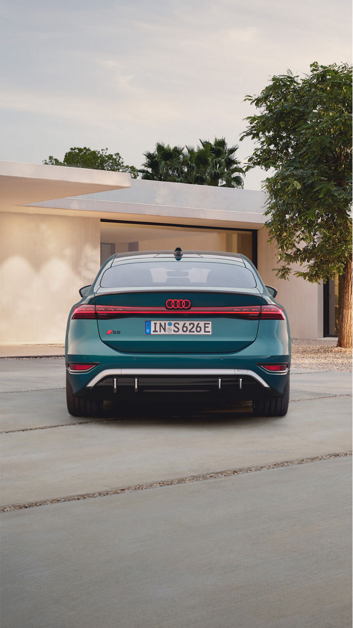 The rear view of a teal Audi S6 Sportback e-tron showcases its sleek design, distinctive taillights, and modern features against a minimalist background. 