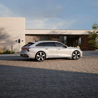 White Audi A6 Avant e-hybrid parked on gravel in front of modern house