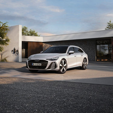 White Audi A6 Avant e-hybrid front view while parked in front of modern house