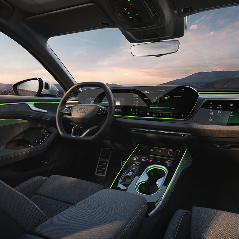 Audi interior showcasing a modern dashboard, green accents, and high-tech displays against a sunset landscape outside.