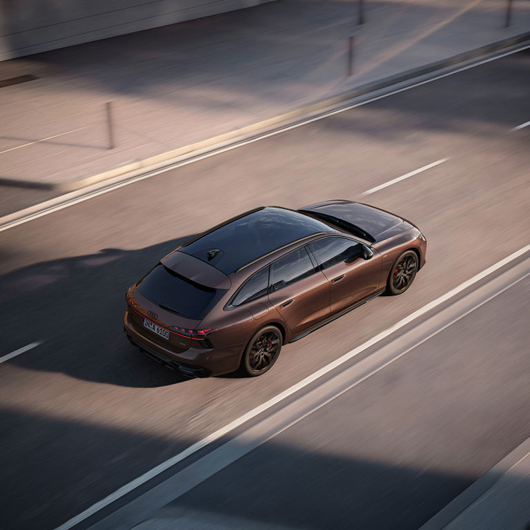 A brown A6 Avant car driving on a city street, exhibiting some motion blur.