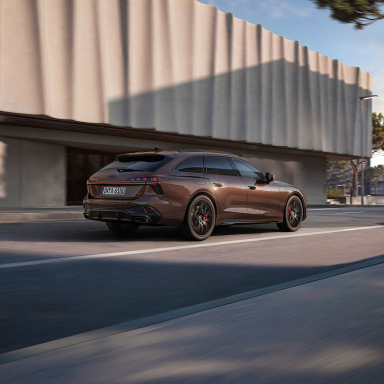 A brown Audi A6 Avant car in motion on a city street with building in the background