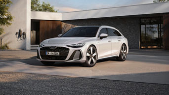 A white Audi A6 Avant e-hybrid parked in front of a modern home, showcasing its sporty design and stylish wheels.