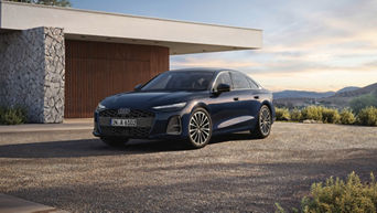 A blue Audi A6 Saloon parked outside a modern home, surrounded by gravel, with mountains and a sunset in the background.