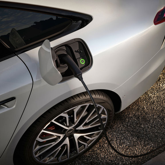 A close-up of an electric car charging port, with a charging cable connected and a green indicator light visible.  