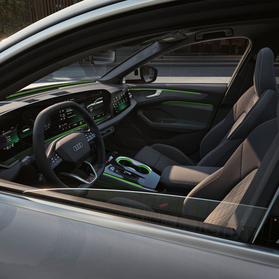Interior view of a modern Audi featuring a sleek dashboard, digital displays, and green ambient lighting. Comfortable grey seats visible.