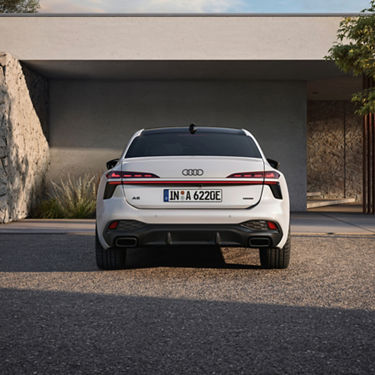 A white Audi car with distinctive headlights is parked under a modern structure, surrounded by greenery.