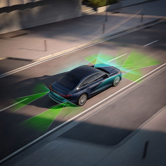 Aerial view of an Audi car with sensor detection zones, near a cyclist on the street.