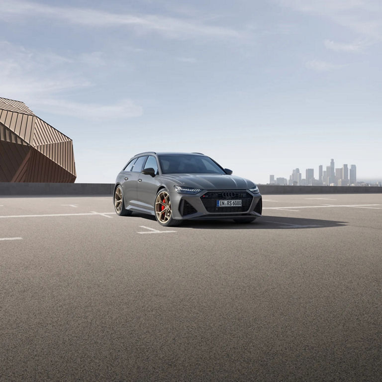 A grey car parked on an empty lot with a city skyline in the background.
