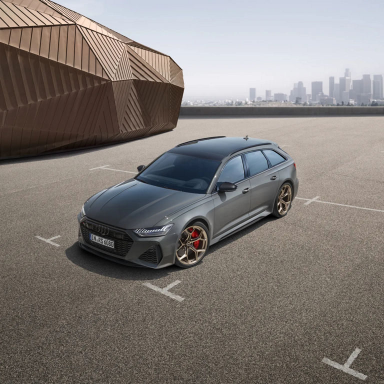 A grey car parked on an open lot with a city skyline in the background.
