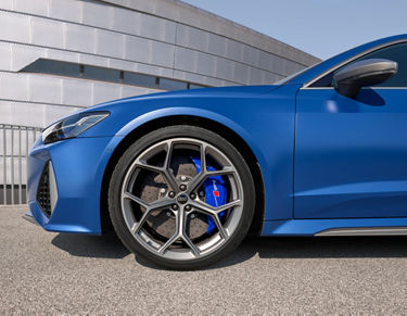 Blue car focusing on wheel with brake callipers, parked outside a building.