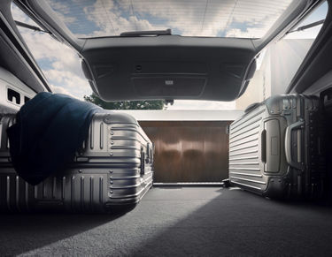 Car trunk open with two suitcases and a jacket, sunlight streaming in.