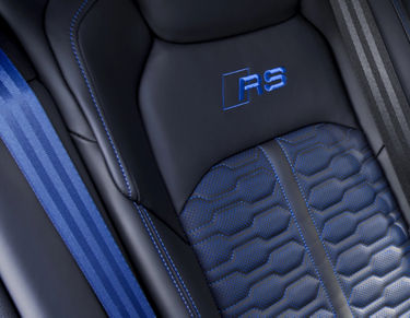 Close-up of a car seat with blue stitching and "RS" embroidery.