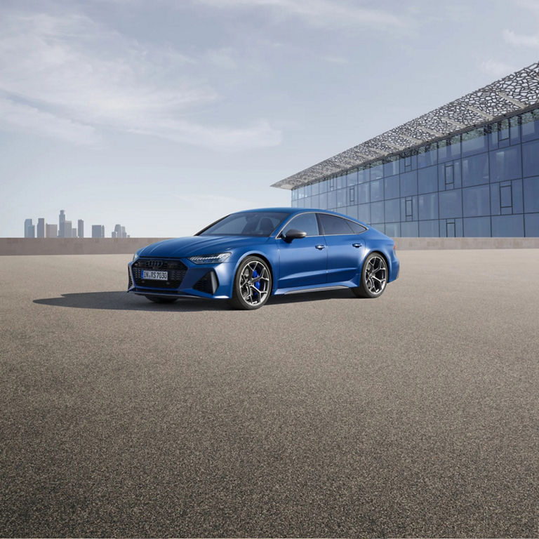 Blue sedan parked outside a modern building with a distant city skyline in the background.