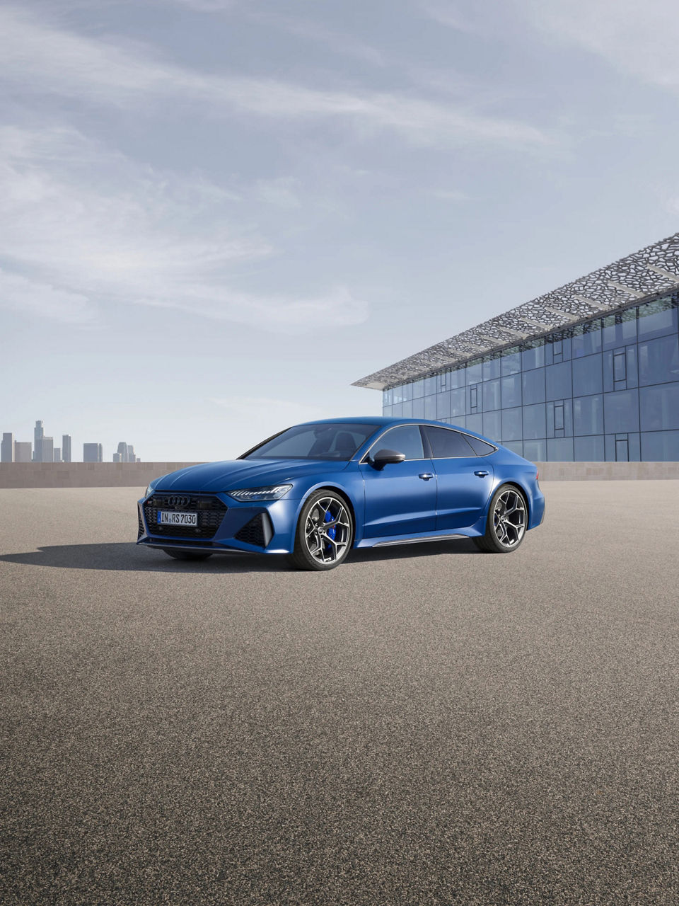 Blue sedan parked outside a modern building with a distant city skyline in the background.