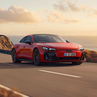 Red Audi e-tron GT cruising down a coastal curvy road