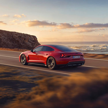A red Audi e-tron GT quattro as seen from the side driving on a coastal road with wavy sea in the background
