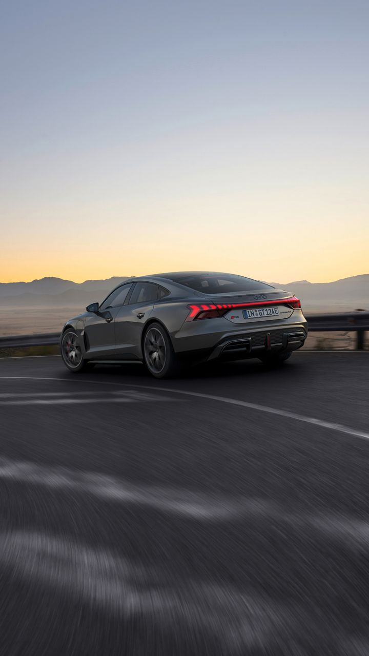 Grey Audi RS e-tron GT driving on highway at dusk with mountainous backdrop.