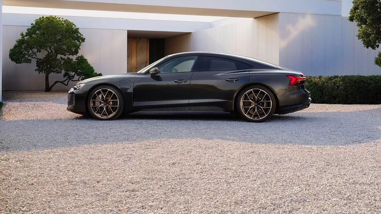 A sleek dark colour luxury sedan parked on a gravel driveway, surrounded by modern architecture and greenery.