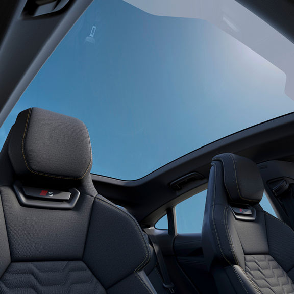 Interior view of RS e-tron GT with stylish RS-model seats and a panoramic sunroof, revealing a clear blue sky above.