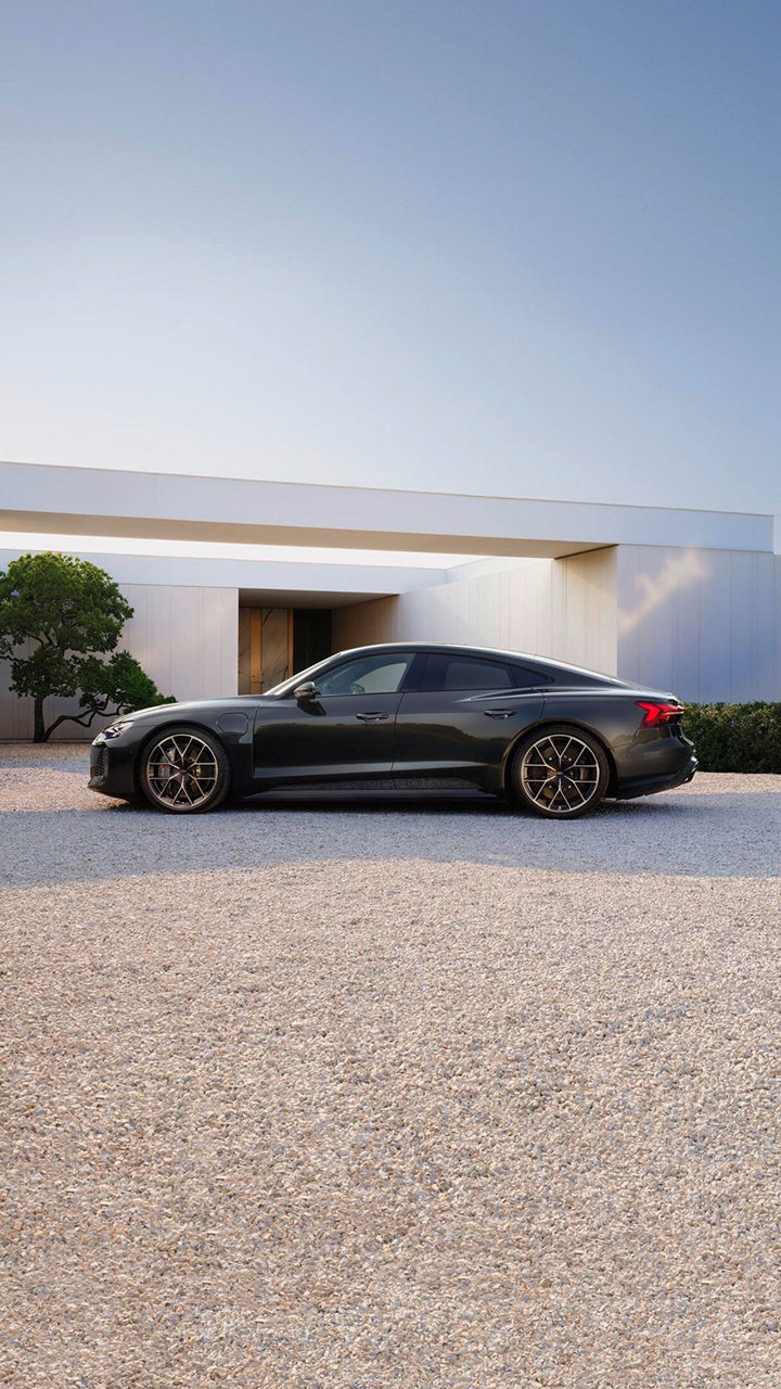 A sleek dark colour luxury sedan parked on a gravel driveway, surrounded by modern architecture and greenery.