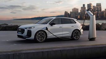 A white Q3 SUV e-hybrid is being charged at a modern charging station, set against a scenic waterfront city skyline at dusk.