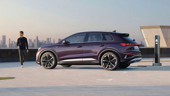 A purple Q4 e-tron parked beside a charging station, with a city skyline in the background during sunset.