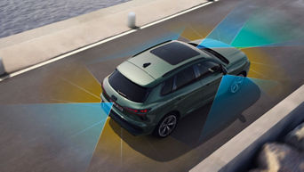 A green SUV drives along a waterfront road, surrounded by colourful sensor lines indicating advanced safety features.