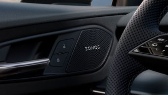 Close-up of a car's interior featuring a Sonos speaker and control buttons on the door panel, with a textured steering wheel in view.