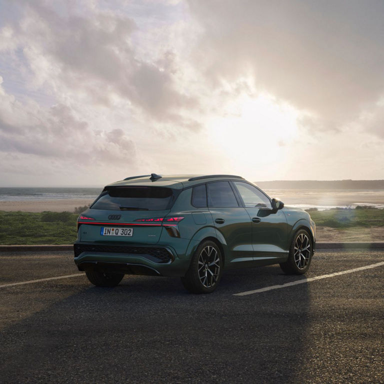 Green Audi SUV parked by the beach at sunset, showcasing its modern design against a tranquil ocean backdrop.