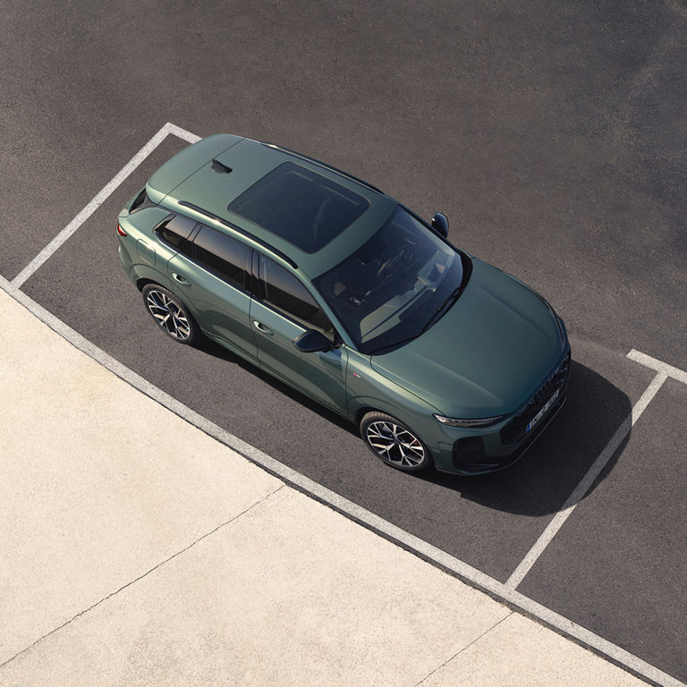 Aerial view of a green SUV parked neatly in a defined space on a modern asphalt surface. Sunlight reflects off its stylish design.