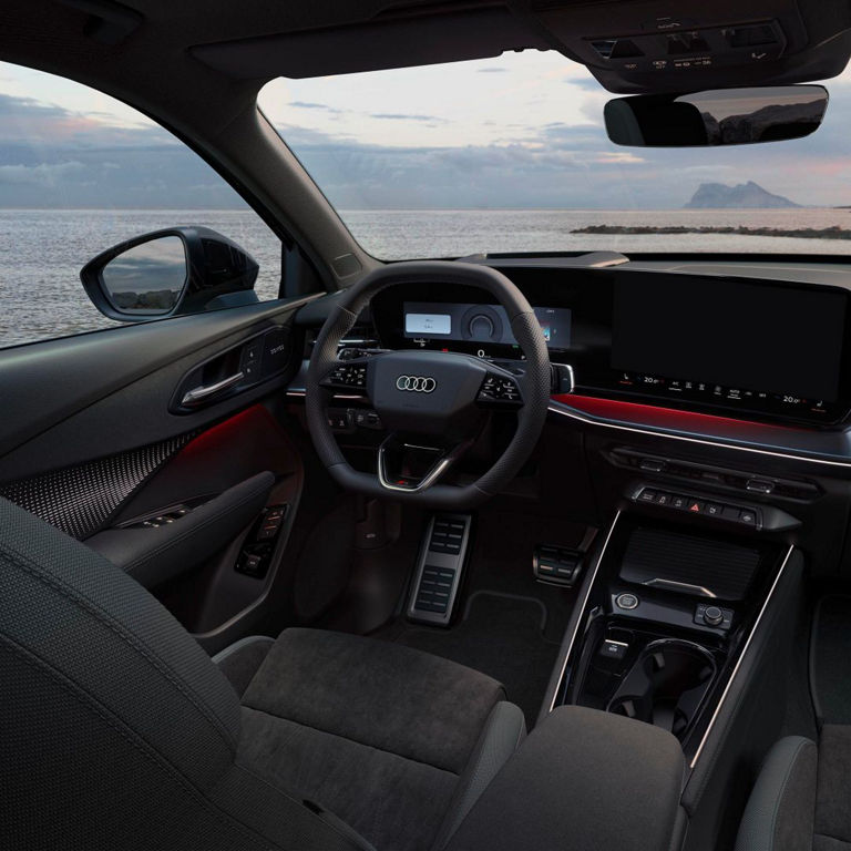 Interior view of a modern Audi car, showcasing a sleek dashboard, steering wheel, and panoramic ocean view through the window.