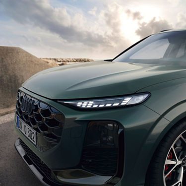 A close-up of a dark green Audi Q3, showcasing its sleek design, modern headlights, and a scenic coastal backdrop.
