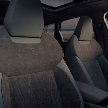 Interior view of modern car seats featuring a sleek design with black suede and grey accents, highlighting the 'S' logo emblem.